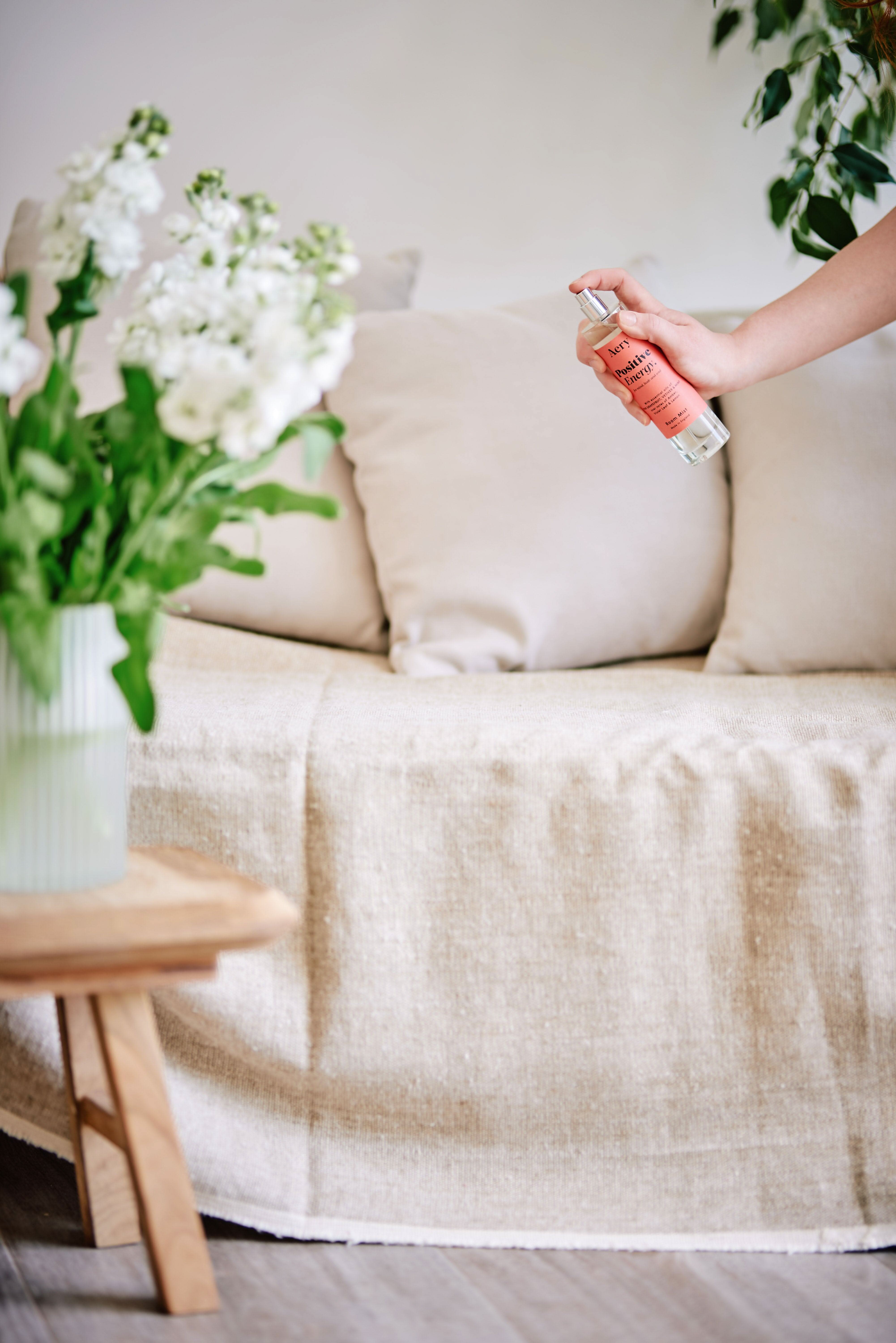 Orange Positive Energy room mist by Aery displayed in hand with vase of white flowers