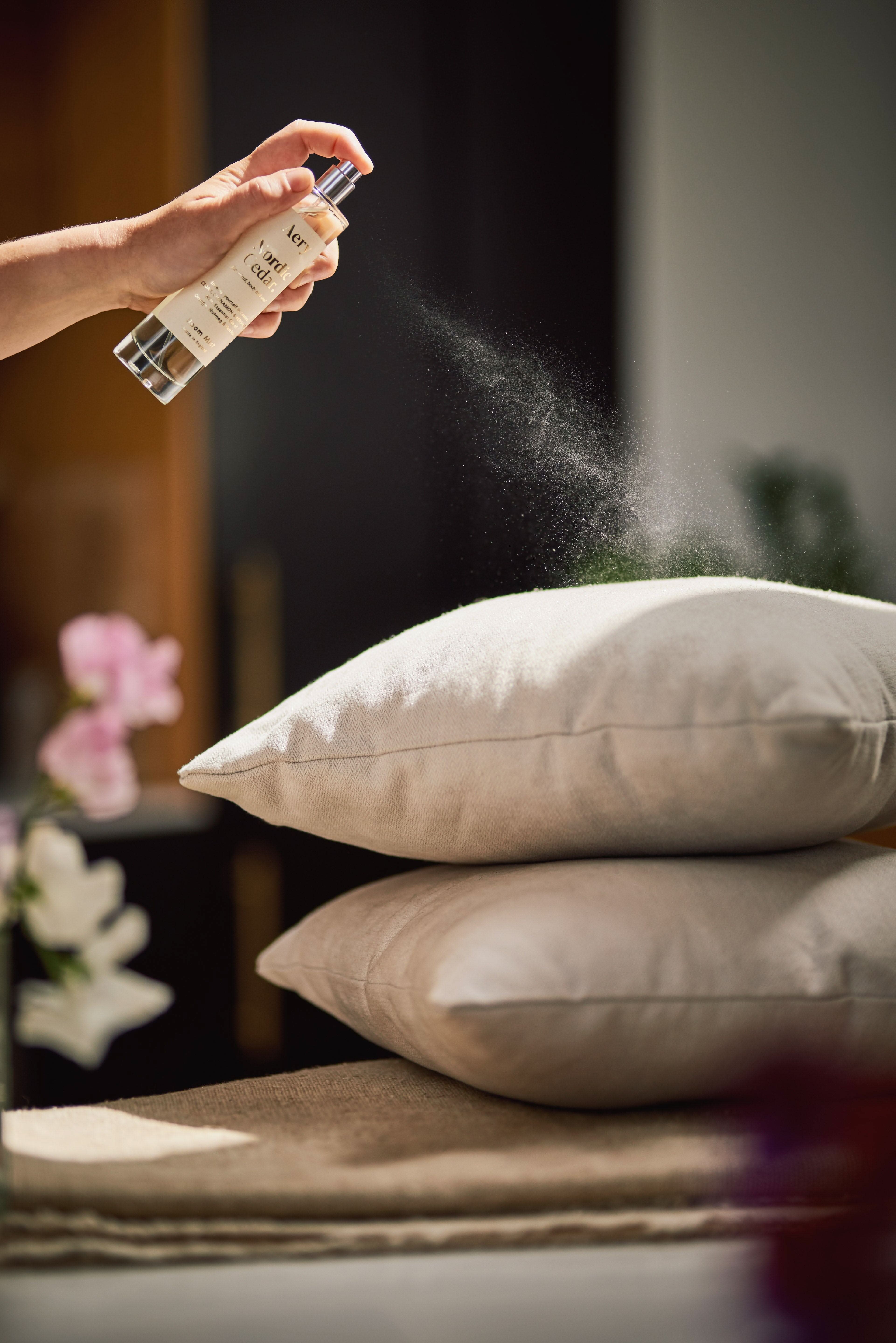 White Nordic Cedar room mist by Aery displayed in hand spraying grey pillow