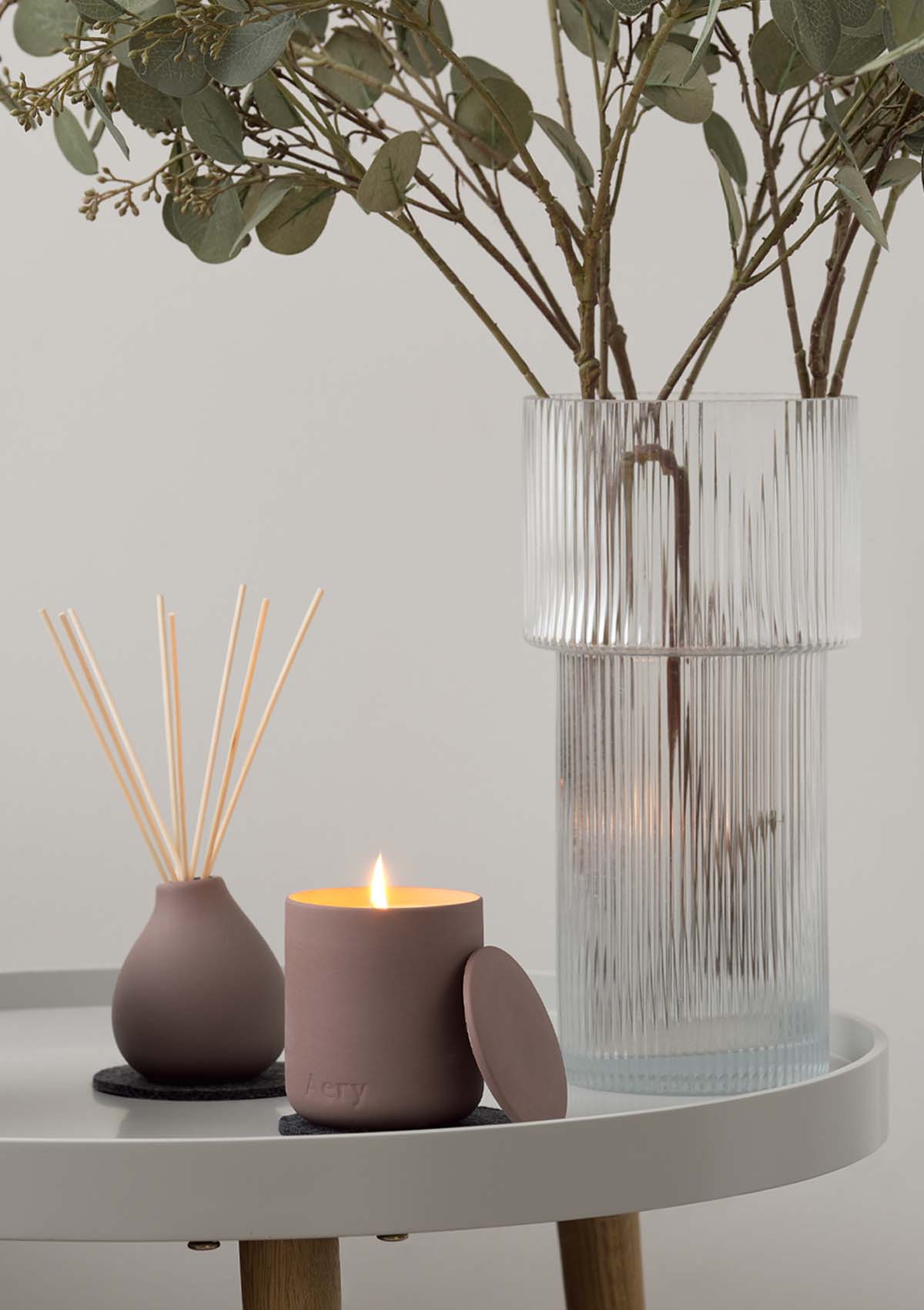 Aubergine moroccan Rose candle by Aery displayed next to Aubergine Moroccan Rose reed diffuser by Aery and glass vase placed on grey circle table