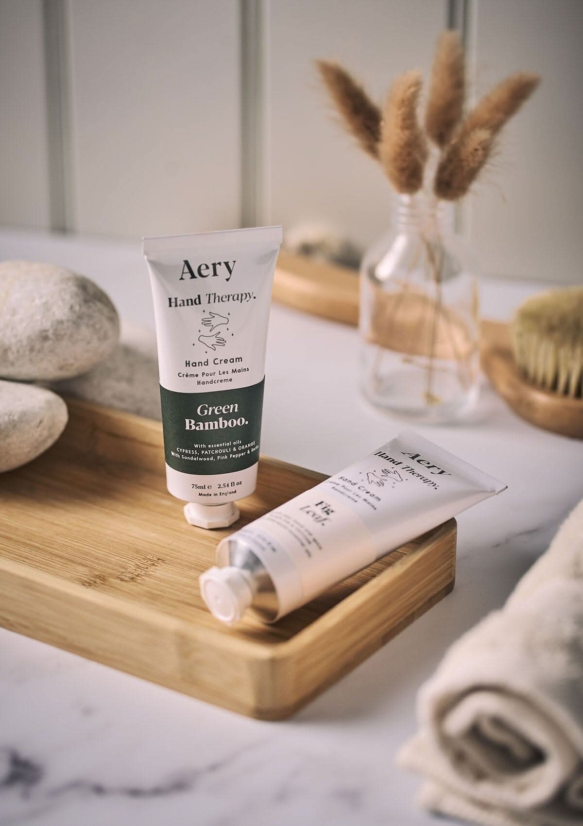 Fig Leaf hand cream by Aery displayed next to Green Bamboo hand cream displayed on wooden tray in bathroom